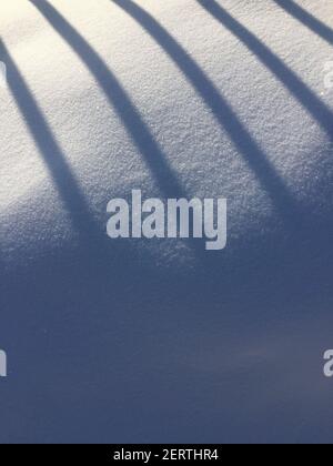 the shadow of the fence on the snow on a sunny day. diagonal parallel lines of shade on white Stock Photo