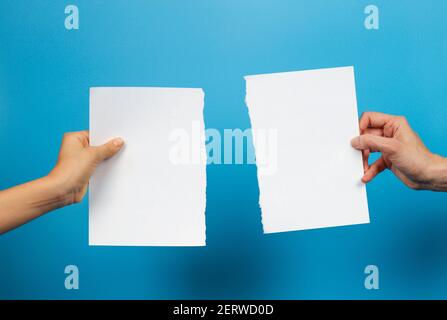 Kid and woman hands holding pieces of torn white paper sheet on light blue background Stock Photo