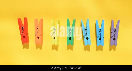 Mood-boosting color concept, multi-colored wooden multi-colored clothespins in a row on a yellow paper background. Creative minimalistic design, flat Stock Photo