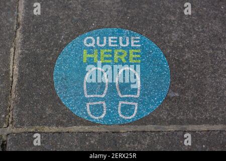 A sign on the pavement outside a supermarket showing people where to stand to keep social distance during the coronavirus pandemic Stock Photo