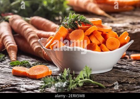 Sliced pieces of carrot in a bowl and a fresh bunch of carrots in the background Stock Photo