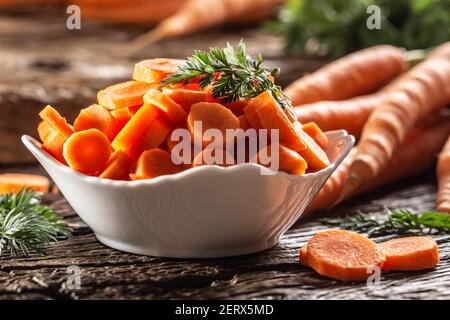 Sliced pieces of carrot in a bowl and a fresh bunch of carrots in the background Stock Photo