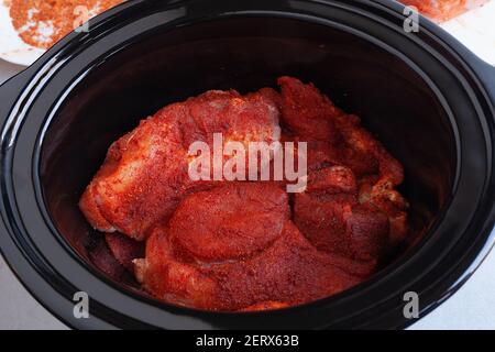 Raw meat covered in spices and dry rub, ready for cooking in slow cooker, placed in black clay pot Stock Photo