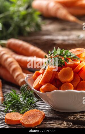 Sliced pieces of carrot in a bowl and a fresh bunch of carrots in the background Stock Photo