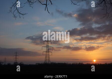 Sunset with silhouetted high voltage electricity pylons of the National Grid, in Norfolk, England, UK. Stock Photo