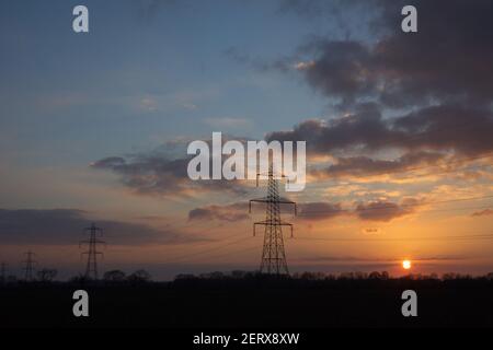 Sunset with silhouetted high voltage electricity pylons of the National Grid, in Norfolk, England, UK. Stock Photo