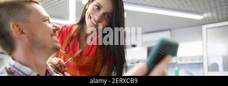 Woman hairdresser smiles and holds hair clipper in her hands and communicates with client. Stock Photo