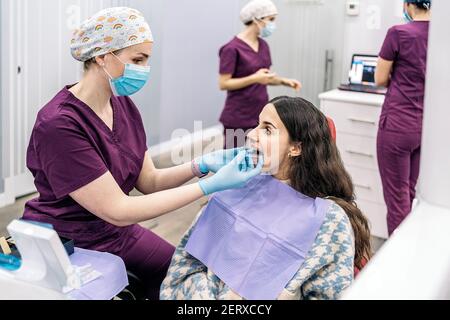 Stock photo of woman sitting in dentist's chair putting on teeth covers. Stock Photo