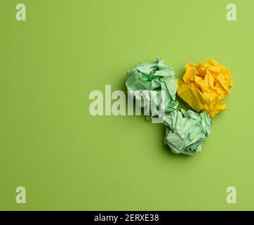 three crumpled balls of colored paper on a green background, copy space Stock Photo
