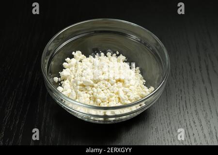 Grainy cottage cheese in a glass bowl on a black background close-up Stock Photo