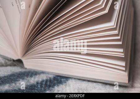 A macro image of book pages and cover of a hardback book on top of a blanket on a surface. Stock Photo