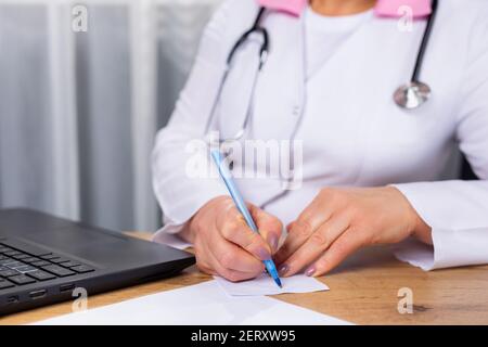 Cropped photo of a doctor therapist sitting at a table in front of a computer. Record of the correct liching. Preparations. Recipe. Stock Photo