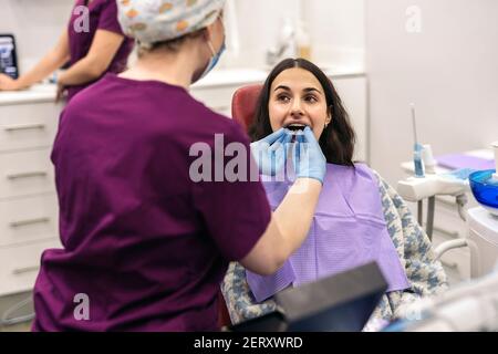 Stock photo of woman sitting in dentist's chair putting on teeth covers. Stock Photo