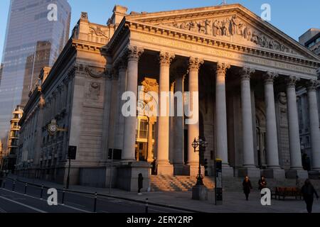 With modern offices of financial institutions behind, an architectural sunlit view of the friezes and Latin inscriptions on the pediment of the Royal Exchange in the City of London, the capital's financial district, on 27th February 2021, in London, England. At the top of Doric and Ionic columns with their ornate stonework, powerfully strong lintels cross, bearing the load of fine artistry and carvings which feature the design by Sir William Tite in 1842-1844 and opened in 1844 by Queen Victoria whose name is written in Latin (Victoriae R). It’s the third building of the kind erected on the sa Stock Photo