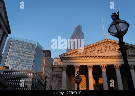 With modern offices of financial institutions behind, an architectural sunlit view of the friezes and Latin inscriptions on the pediment of the Royal Exchange in the City of London, the capital's financial district, on 27th February 2021, in London, England. At the top of Doric and Ionic columns with their ornate stonework, powerfully strong lintels cross, bearing the load of fine artistry and carvings which feature the design by Sir William Tite in 1842-1844 and opened in 1844 by Queen Victoria whose name is written in Latin (Victoriae R). It’s the third building of the kind erected on the sa Stock Photo