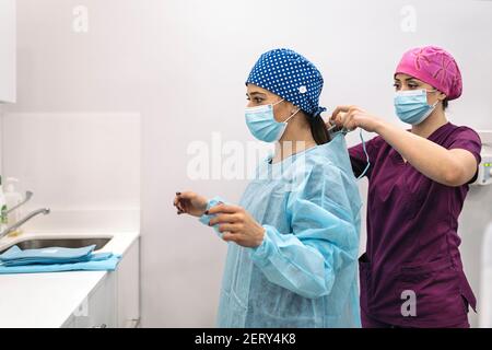 Stock photo of woman wearing face mask and hair net helping her coworker in a dental clinic. Stock Photo