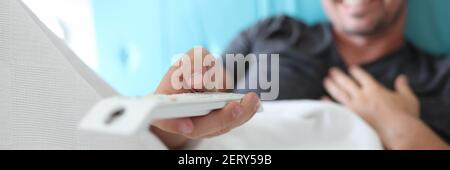 Man lies on bed and holds remote control in his hands. Stock Photo