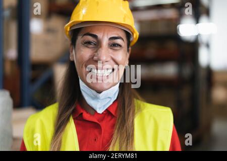 Happy Latin woman working in warehouse while wearing face mask during corona virus pandemic - Logistic and industry concept Stock Photo