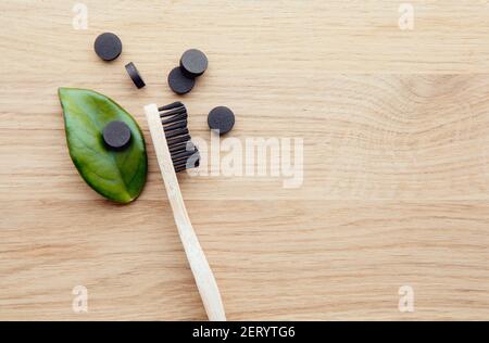 Black activated charcoal toothpaste tablets. Dental care concept. Natural ingredients, top view of bamboo toothbrush with black toothpaste tablets. Stock Photo
