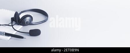 Headset, checkered notebook and ballpoint pen on a light background. Toning in gray-blue. Stock Photo