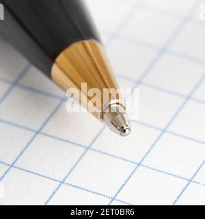Close up of the tip of a ballpoint pen on the background of a sheet of checkered paper Stock Photo
