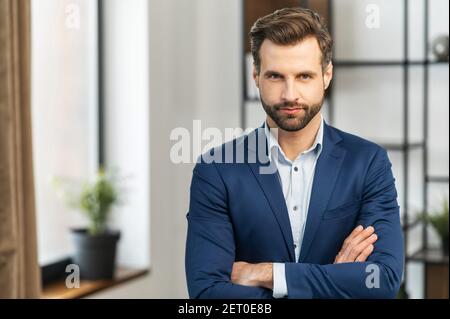 Successful serious authoritative confident young bearded brunet adult male entrepreneur businessman professional in formal wear standing with arms cro Stock Photo