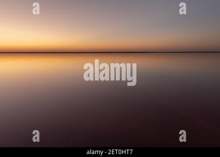 Tranquil minimalist landscape with smooth surface of the pink salt lake with calm water with horizon with clear sky in sunset time. Simple beautiful natural calm background Stock Photo