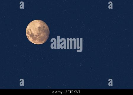 Full moon at dusk glowing against blue starry sky dark background Stock Photo