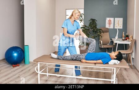 Physiotherapist treating leg injury on a little boy lying down. African American child training with his therapist Stock Photo