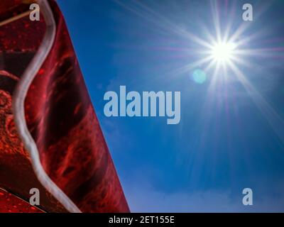 A red parasol against almost clear blue sky with sun and sun flare Stock Photo