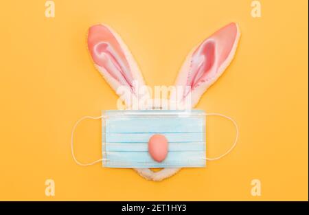 Happy Easter during the Coronavirus time! Rabbit ears and face mask on yellow background. Stock Photo