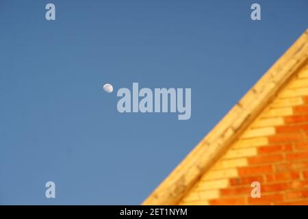 Brick house roof and growing moon in clear blue sky during the day Stock Photo