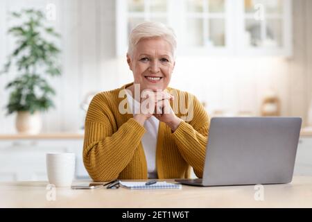 Happy elderly lady waiting for webinar, using laptop Stock Photo