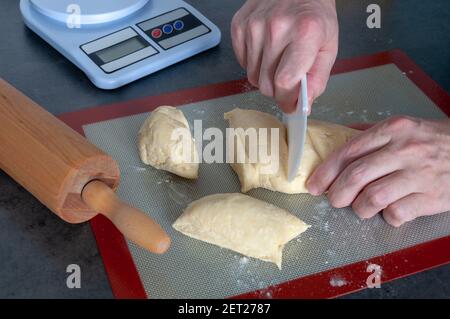 Rolling pin, a flexible plastic cutter, weighing machine. Hands cutting the dough. Stock Photo