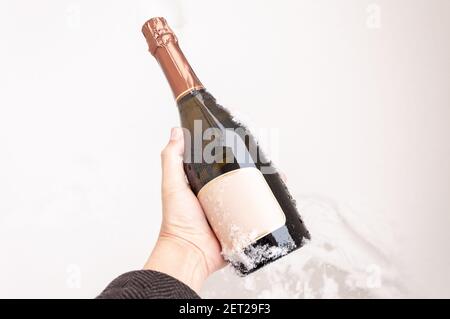 A bottle of chilled sparkling wine in hand against a background of white snow. Stock Photo