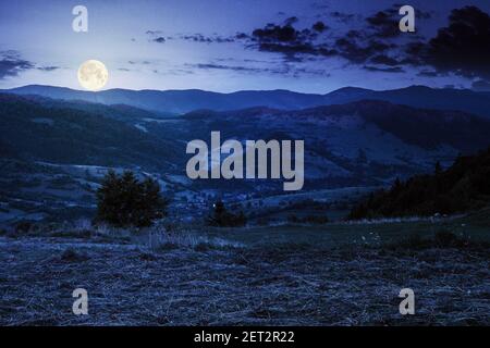 mountainous rural landscape at night. grassy meadow on top of a hill. clouds above the ridge in full moon light. view in to the distant valley Stock Photo