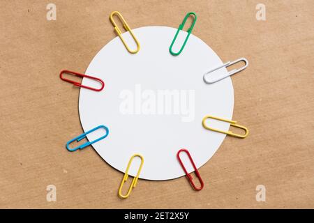 white circle with colored paper clips. Brown background from kraft paper. Stock Photo