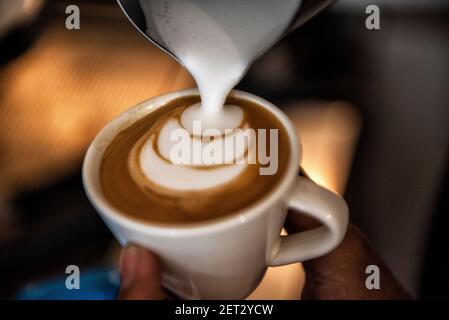Close-up of a person pouring microfoam on a piccolo latte coffee drink to make a decorative pattern Stock Photo