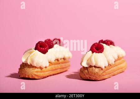 Two colorful eclairs laying on pink background. French sweet dessert. Homemade pastry. Stock Photo