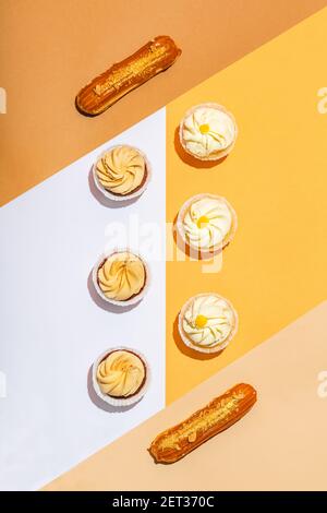 Flat lay composition of sweet desserts. Bright, warm colors. Cupcakes and eclairs, pastry. Stock Photo