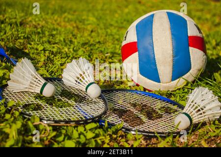 Three shuttlecocks, two badminton rackets and a volleyball ball on the grass. The concept of outdoor sports games Stock Photo