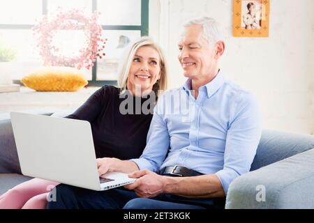 Shot of happy senior couple using notebook while sitting together on the sofa at home. Stock Photo