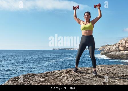 Latin woman, middle-aged, wearing sportswear, training, doing physical exercises, plank, sit-ups, climber's step, burning calories, keeping fit, outdo Stock Photo