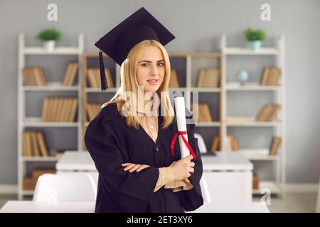 Serious university graduate standing in classroom, holding diploma and looking at camera Stock Photo