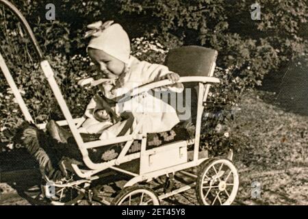 Latvia - CIRCA 1940s: Portrait of baby girl sitting in carriage. Baby stroller pram. Vintage archive Art Deco era photography Stock Photo