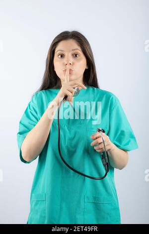 Portrait of a young woman doctor with stethoscope in uniform showing silent sign Stock Photo