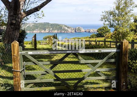 The beautiful rugged south coast of Guernsey seen across the garden of a thoughful landowner - A glimpse of Saints Bay from the Icart Road, Guernsey, Stock Photo