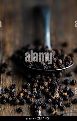 Spoonful of black peppercorns on a  wooden table Stock Photo