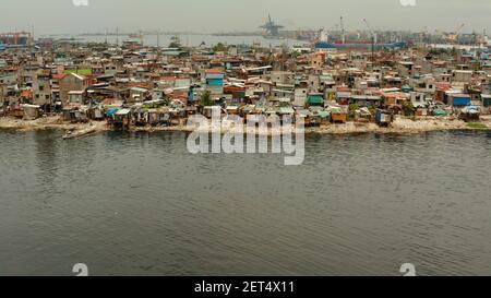 Slums in Manila near port on the bank of a river polluted with garbage, aerial view. Stock Photo