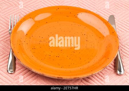 Orange empty plate with knife and fork on pink cotton towel. Stock Photo